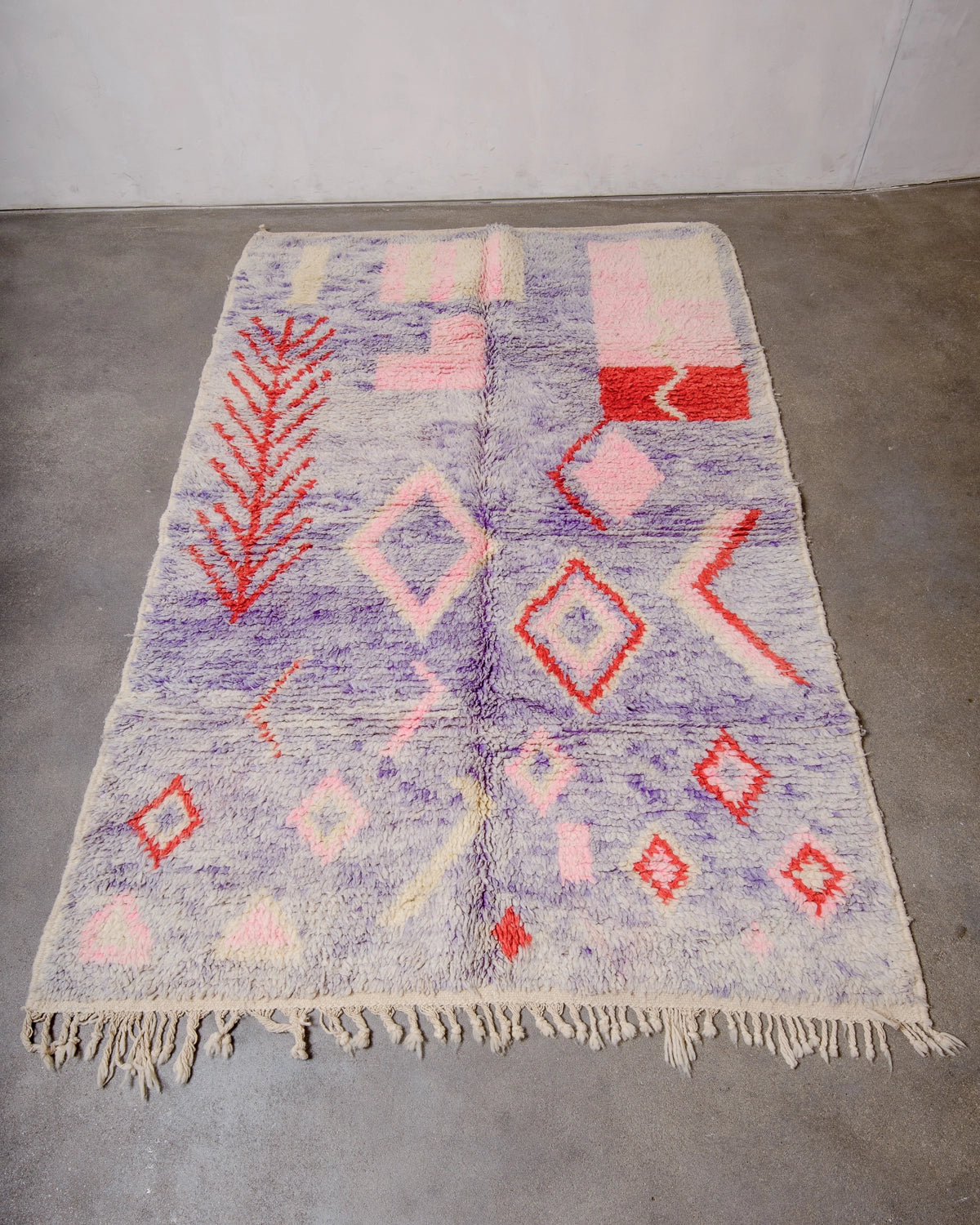 Berberlin Vintage Berber Rug made of fluffy lavender, red, pink and cream wool laying on concrete floor.